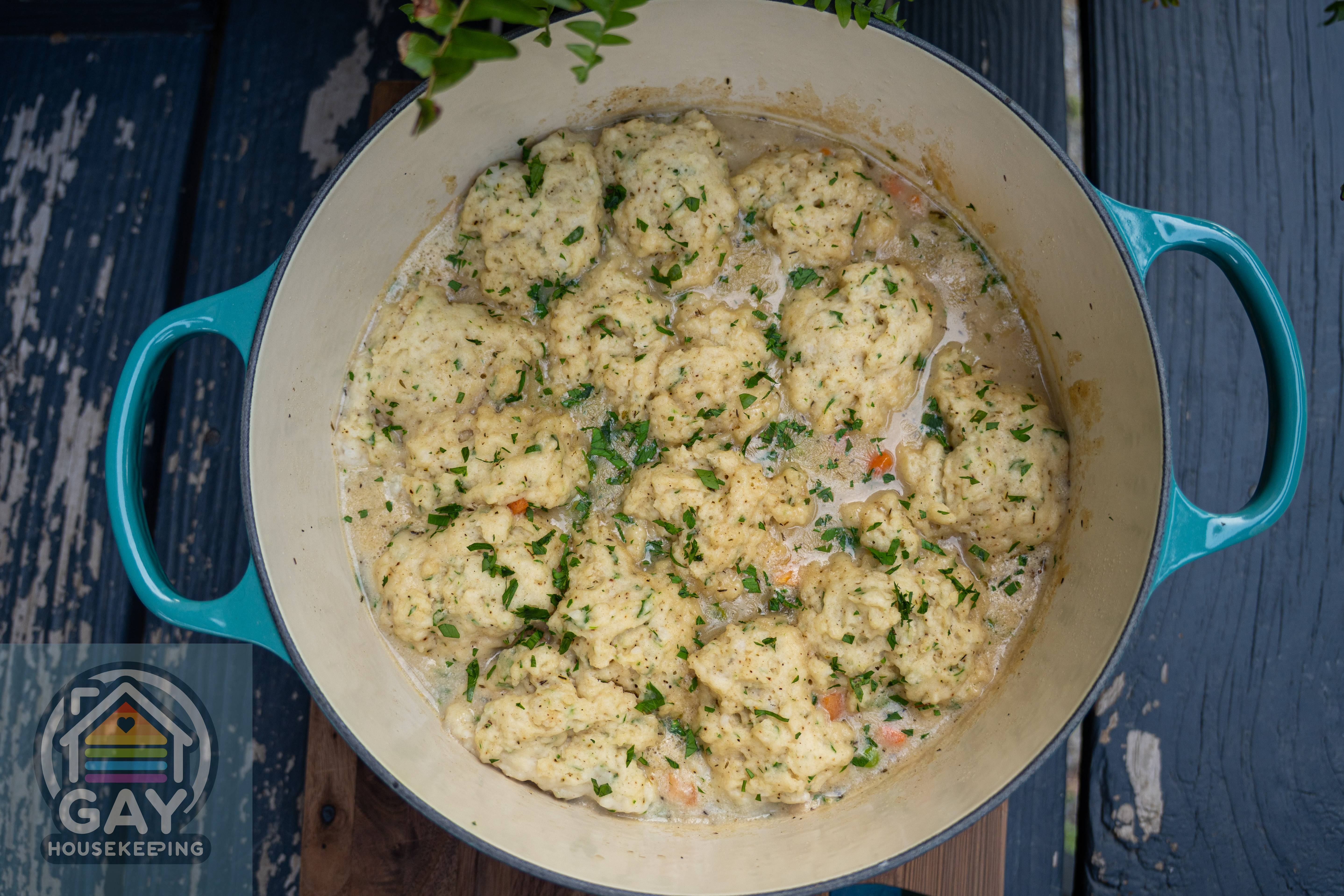 Homemade chicken and dumplings with parsley in a turquoise Le Creuset Dutch oven.