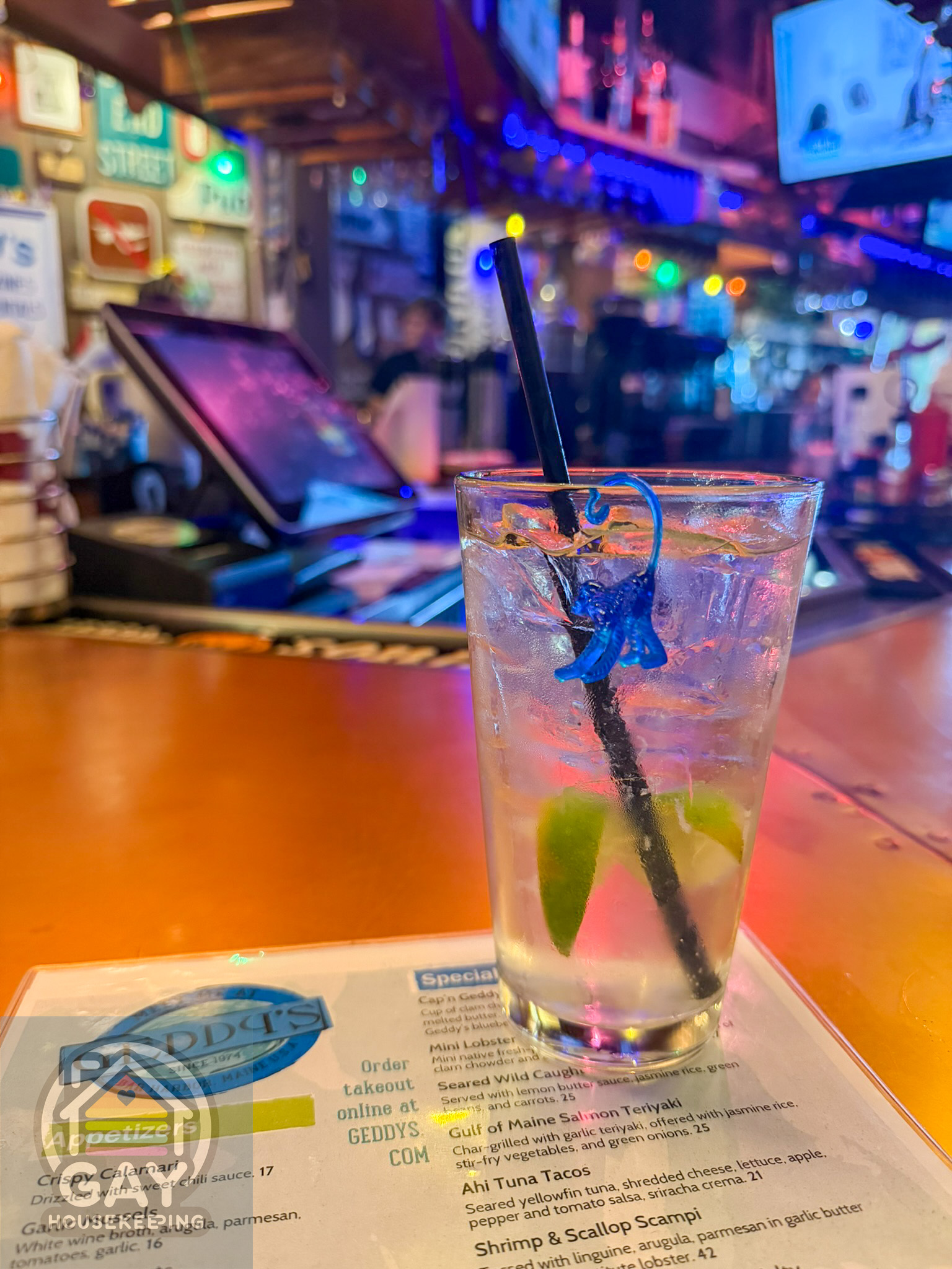 A cocktail at Geddy's with a tiny blue plastic monkey clinging to the straw, the bar glowing behind it.