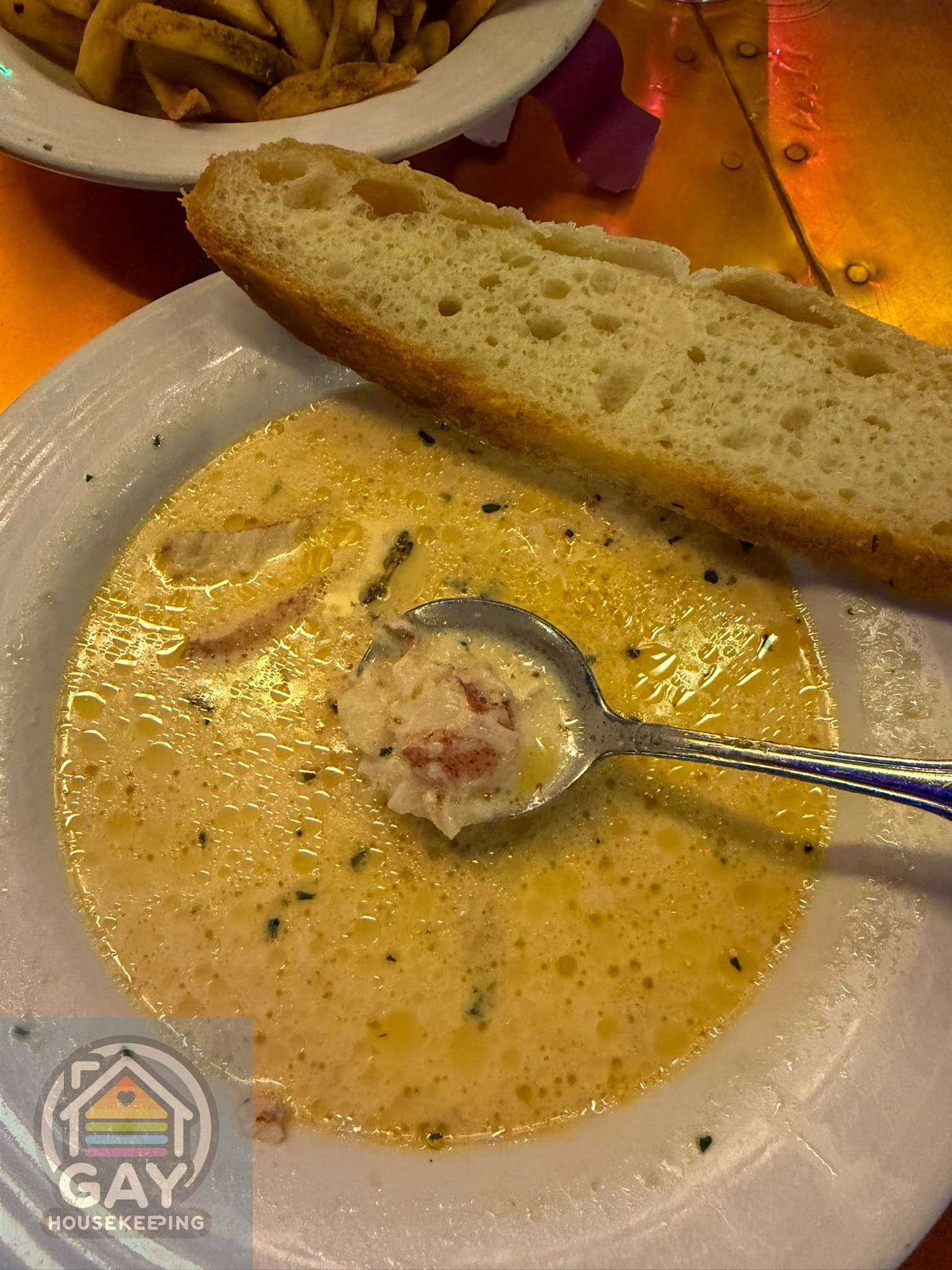 A bowl of creamy lobster bisque with a slice of baguette, fries waiting in the background.