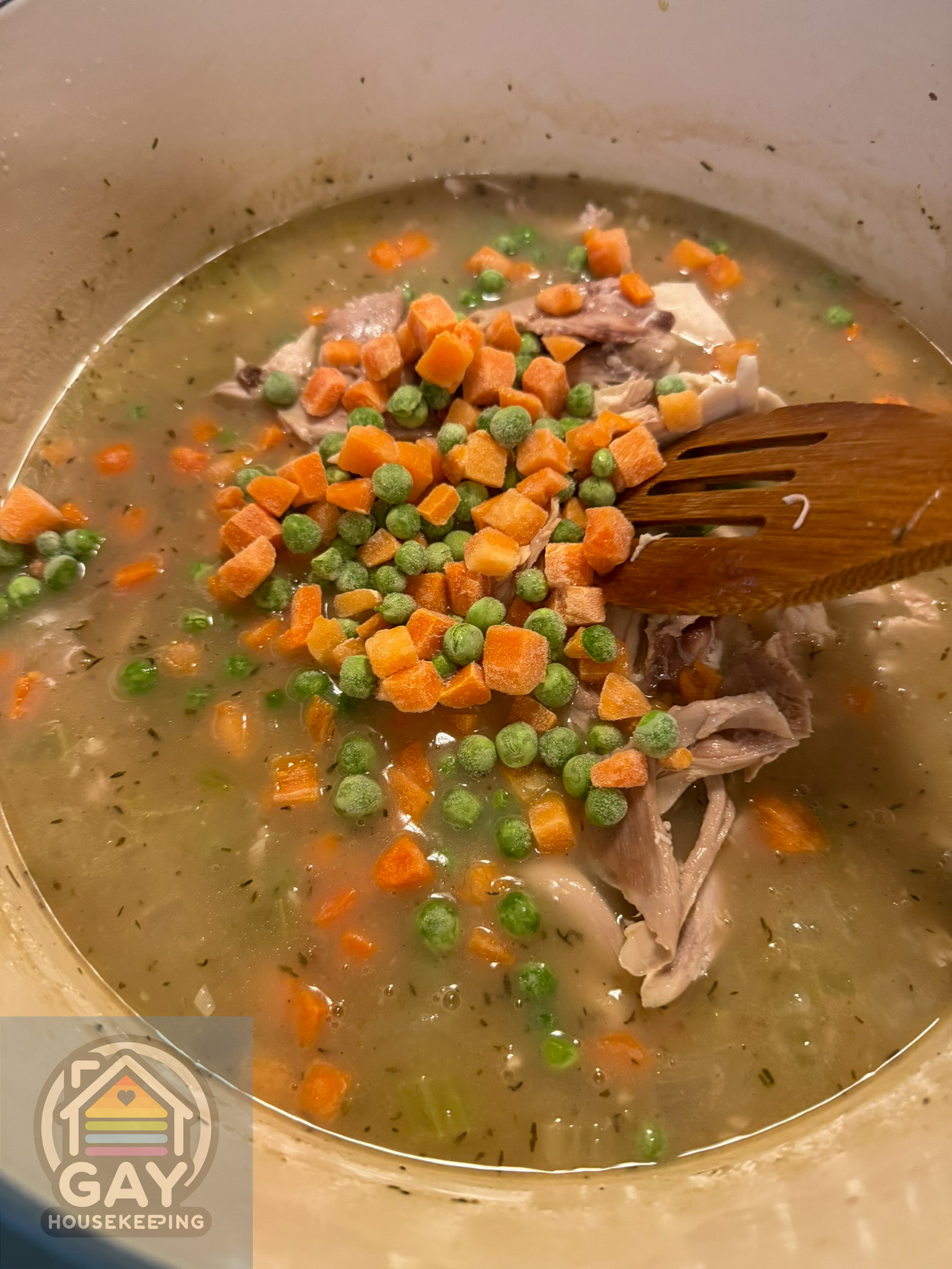 Pulled chicken, frozen peas and diced carrots going into the thickened broth.