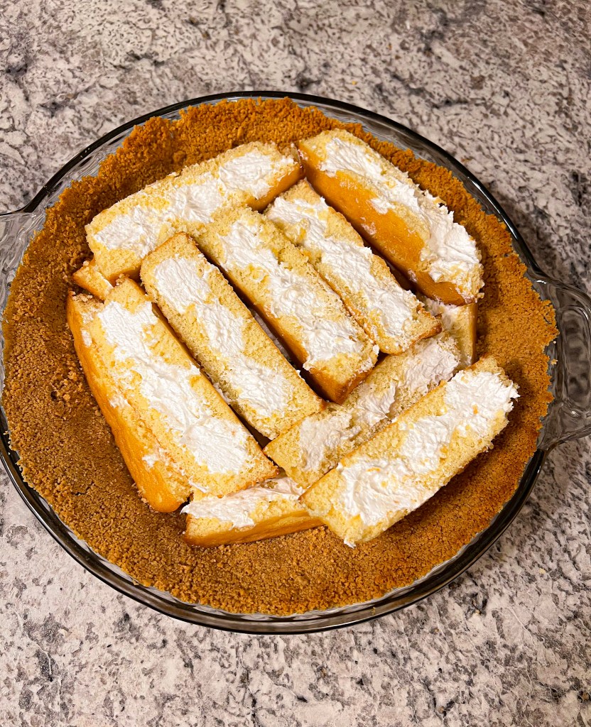 Twinkies lined up on a graham cracker crust in a glass pie dish, prepped for pie assembly.