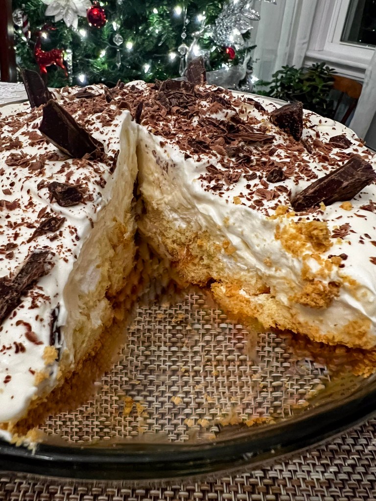 A slice of Twinkie pie with whipped cream and chocolate shavings on top, with one piece lifted out to reveal the layers.
